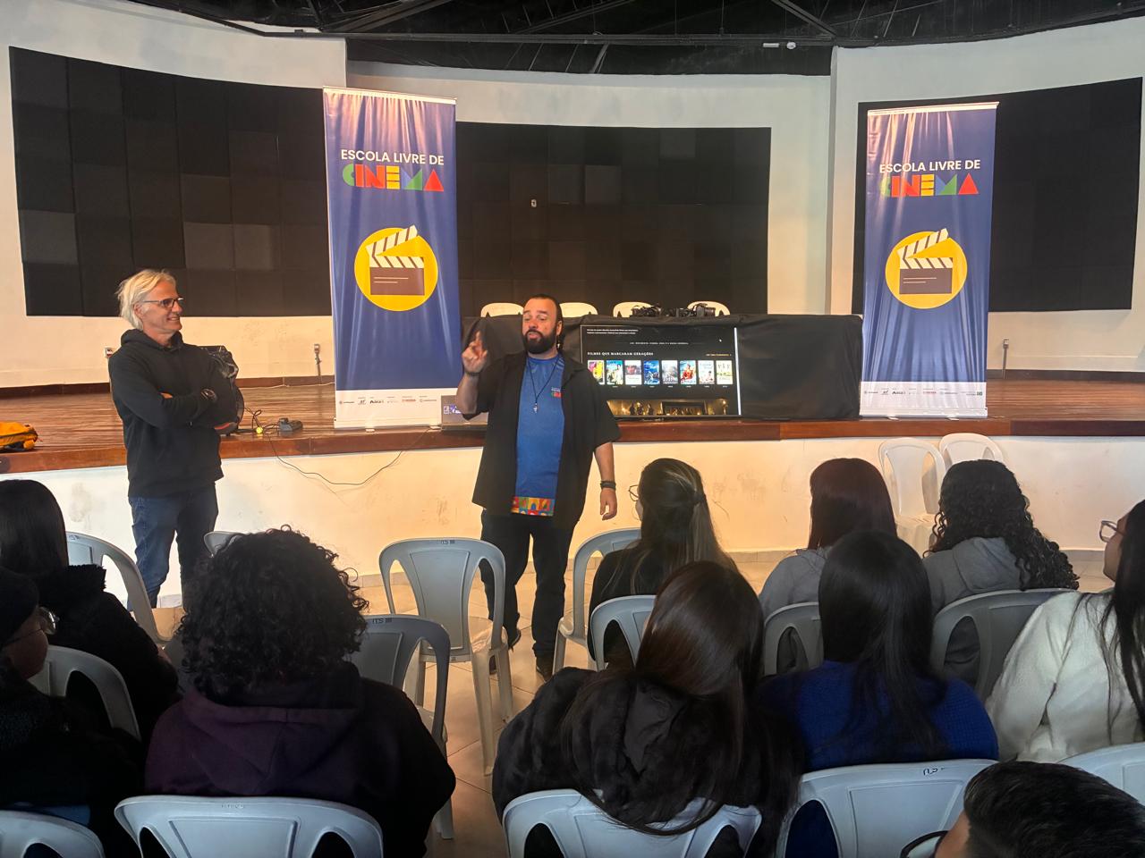 Marcelo Torres em atividade do workshop inaugural da Escola Livre de Cinema, diante de estudantes em um auditório em Extrema, Minas Gerais.